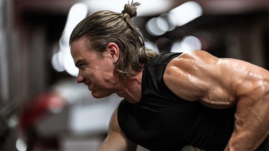 Mies ponnistelee treenatessaan.  Mies ponnistelee treenatessaan.